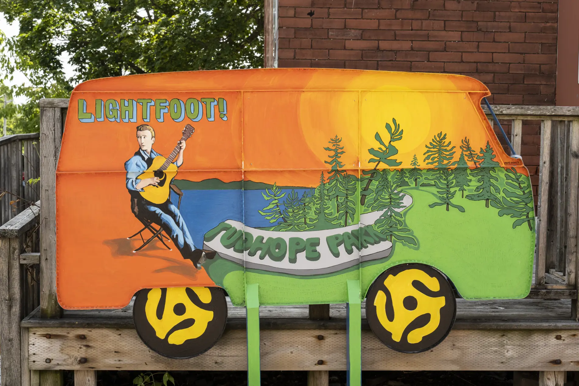 A hand painted sculpture of a vintage van depicts musician Gordon Lightfoot playing guitar by a lake