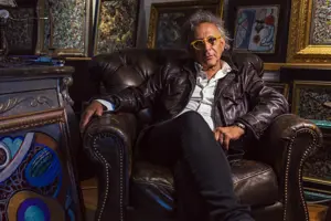 Musician Marc Jordan Posing On A Brown Leather Chair Surrounded By Various Abstract Paintings